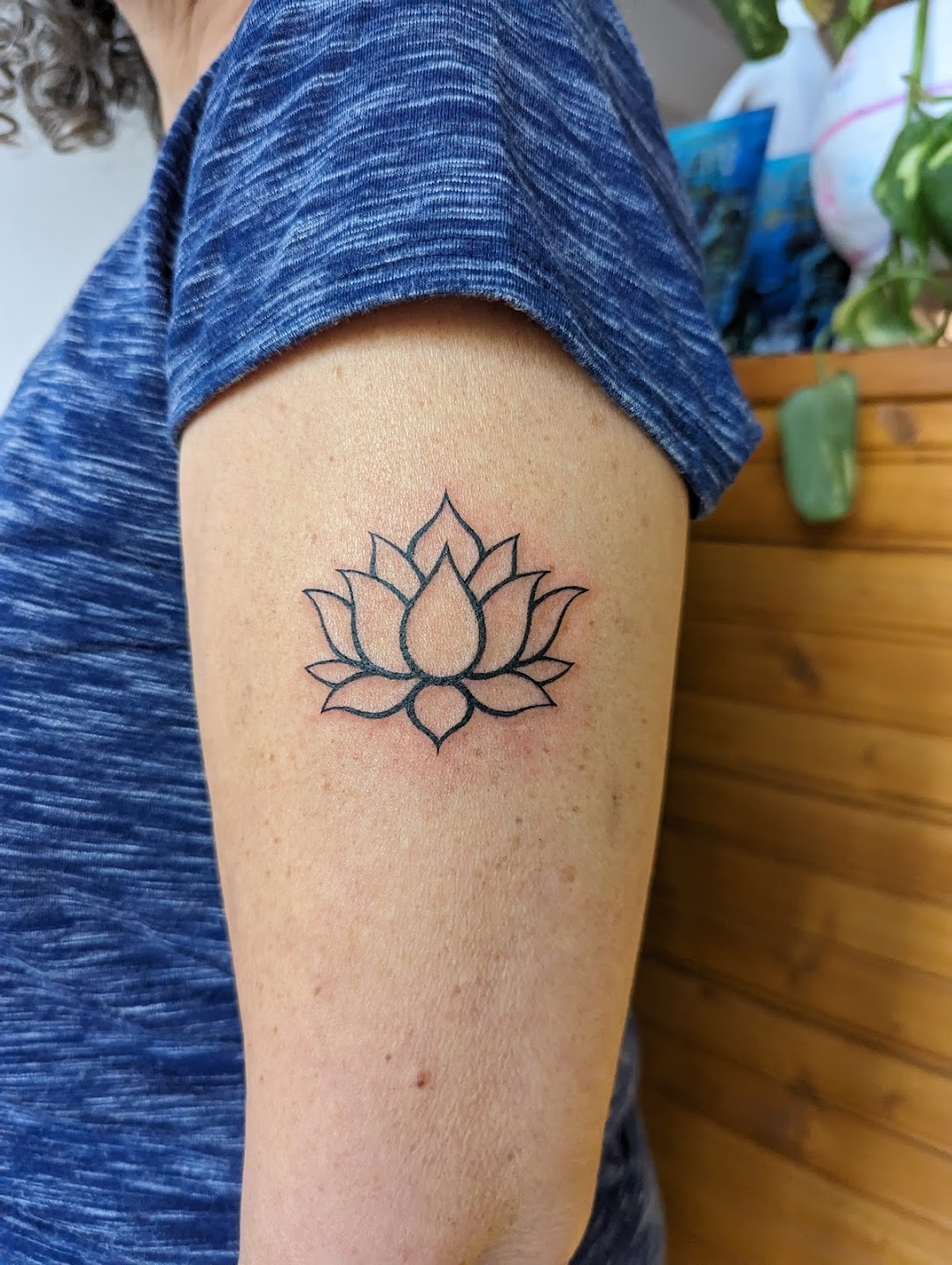 Minimalist lotus outline tattoo on upper arm
